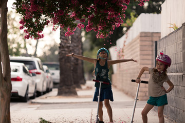 Girls are wearing safety helmets while scootering on the sidewalk of their LA city.