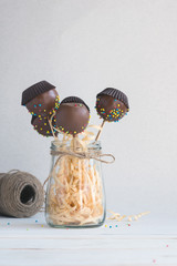 Chocolate cake pops with coconut flakes on a light background. Mini cakes on a wooden stick. A popular sweet dessert.