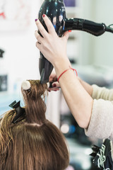 A vertical closeup shot of a hairdresser blow drying a woman's short hair in a beauty salon