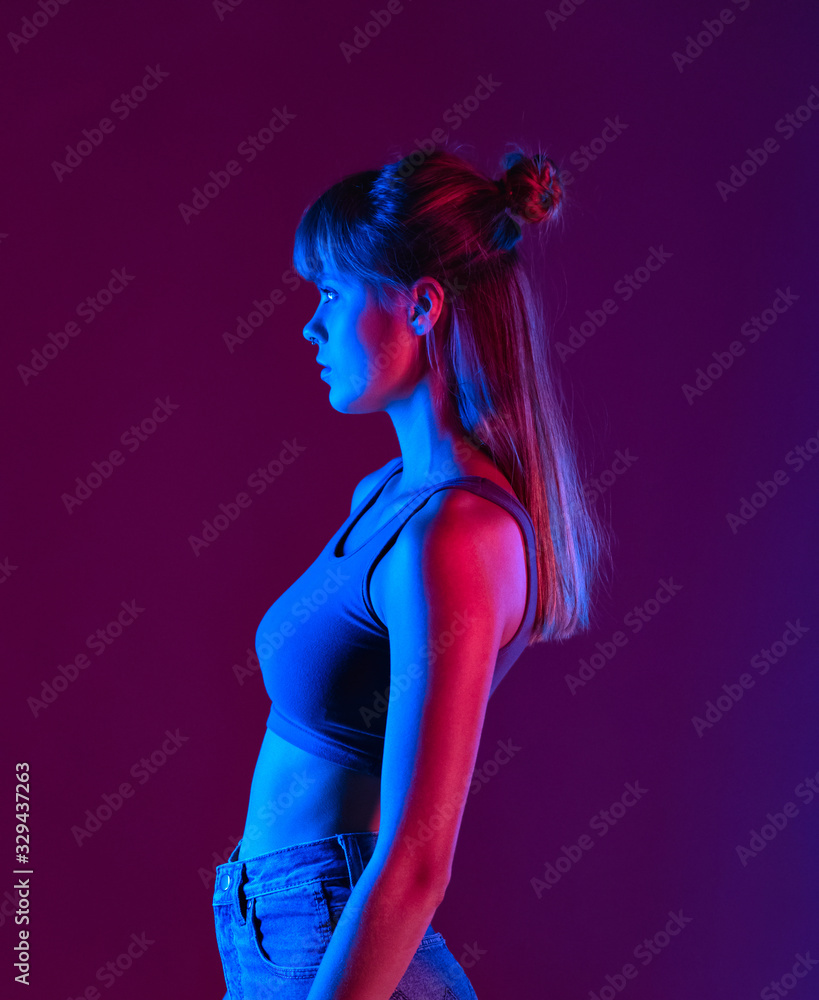 Wall mural Fashion beauty young blond hair 20s girl model profile side view stand at purple studio background, sexy trendy stylish woman pretty face in neon blue party night light concept, vertical photo.