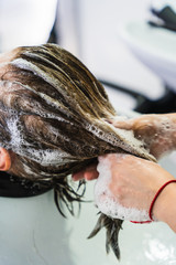 A vertical closeup shot of a hairdresser washing a woman's short hair in a beauty salon