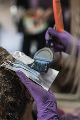 A vertical closeup shot of a hairdresser dying a woman's short hair in a beauty salon