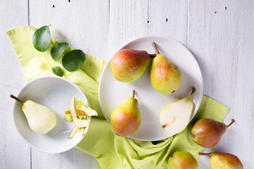 Ripe pears on a light bowl with leaves on a white wooden background. Still life of whole, peeled...