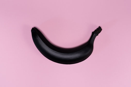 Matte black banana on the pink background. The object is in the centre of the picture. Minimal style. Conceptual minimalism. Matte surface. Fruit. One