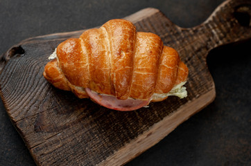 Croissant with sausage, cheese and salad on a stone background