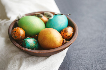 Obraz na płótnie Canvas Bright easter eggs in a clay bowl and fluffy willow branches on a dark background, soft focus. 