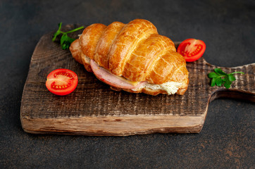 Croissant with sausage, cheese and salad on a stone background