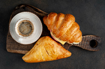 coffee, samsa and croissant with ham and cheese on a cutting board on a stone background