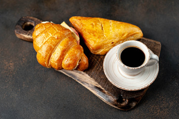 coffee, samsa and croissant with ham and cheese on a cutting board on a stone background