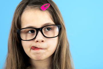 Close up portrait of a funny child school girl wearing looking glasses isolated on blue background.