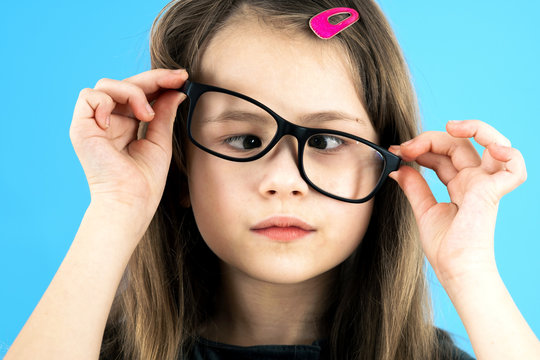 Close up portrait of a cross eyed child school girl wearing looking glasses isolated on blue background.