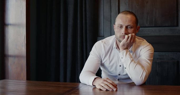 Tired man sitting waiting at a table indoors trying to keep himself from falling asleep jerking himself awake