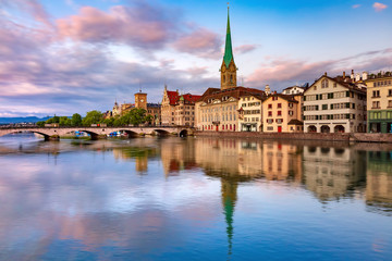 Fototapeta na wymiar Famous Fraumunster church with its reflections in river Limmat at pink sunrise in Old Town of Zurich, the largest city in Switzerland