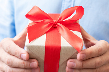 Person holding gift with red ribbon, man's hands, closeup