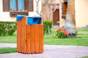 Obraz premium Yellow wooden trash can outdoors on the side of sidewalk in park. Garbage container outside.