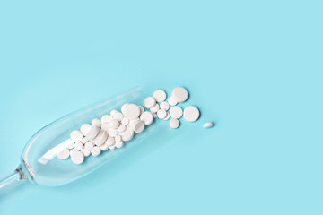 Medical pills in empty wine glass on blue background.
