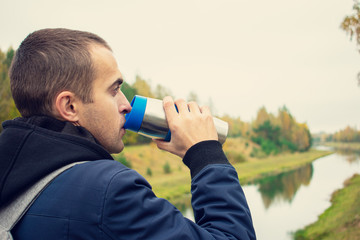 Traveler drinking hot tea from a thermos, a man traveling the world, guy with a backpack on the background of a beautiful landscape, rear view