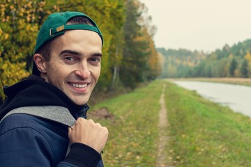 Concept of travel and lifestyle. Guy with a backpack walking along the river.