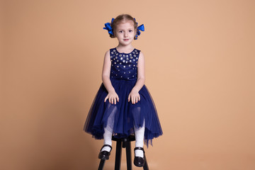 cute little girl sitting on chair in blue dress isolated on beige