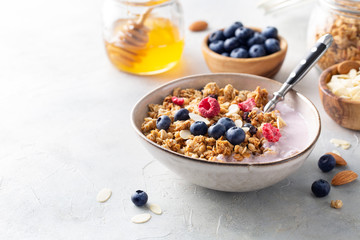 Breakfast. Muesli with yogurt, blueberries, raspberries, almonds and honey on a light background. Space for text.