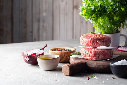 Raw beef steak or minced meat cutlets on a wooden cutting Board, salt, pepper, Greek mini Basil  and oil on the table. Space for text.
