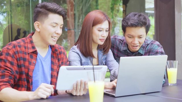 Group of young Asian people using digital tablet and laptop computer while sitting in the cafe. Shot in 4k resolution