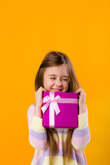 happy little girl with long hair holding a pink gift box on a yellow background isolate