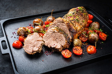 Traditional barbecue rolled lamb roast sliced with tomatoes and mini eggplant as closeup on a...
