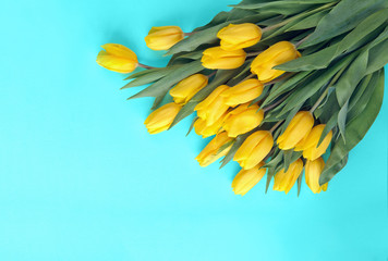 a large bouquet of yellow tulips laid out on a light blue background flat lay