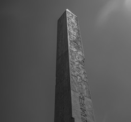 Ancient obelisk is under the clear sky, view from bellow and in black and white technique. We can...