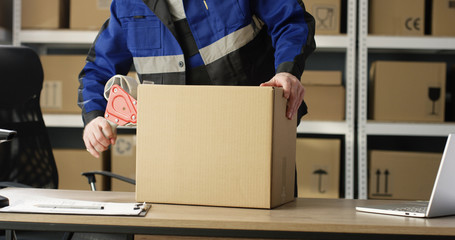 Close up of hands of Caucasian postal male worker in uniform packing carton box at delievery...