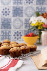 Freshly Baked Strawberry Muffins on Kitchen Counter with Blue and White Backsplash; Muffins on Cooling Rack; Strawberries and Flowers out of focus in Background