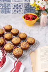 Freshly Baked Strawberry Muffins on Kitchen Counter with Blue and White Backsplash; Muffins on Cooling Rack; Strawberries and Flowers out of focus in Background