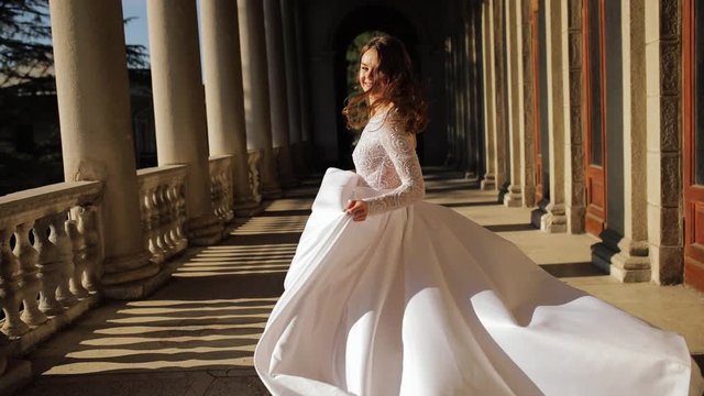 young bride runs on the balcony among the columns on a Sunny day and her dress flutters