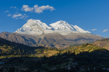 Huascaran mountain in Peru with its two snowy peaks rising over green valley where the town of...