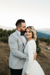 Beautiful couple having a romantic moment on their weeding day, in mountain, sunset.She is in a white wedding dress with a bouquet of sunflowers in hand,groom in a suit. Groom holds bride in his hands