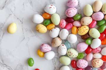 Happy Easter concept. Preparation for holiday. Easter candy chocolate eggs and jellybean sweets on trendy gray marble background. Simple minimalism flat lay top view copy space.