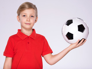 Pretty 8 years old kid in a red t-shirt with a soccer ball in hand.  Photo of a boy in sportswear holding soccer ball, posing at studio. White child holds a soccer ball.