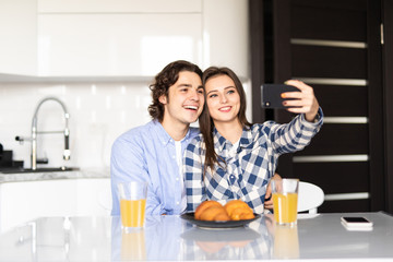 Morning family fun. Portrait of couple drinking coffee in kitchen, using smartphone camera to take selfie.