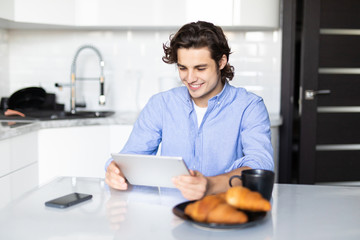 Young man eating breakfast while using digital tablet in modern kitchen
