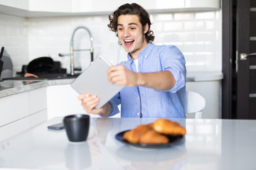 Young pretty man play games on tablet while having breakfast in the kitchen