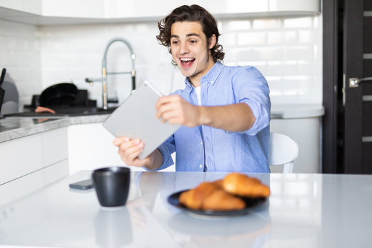 Young pretty man play games on tablet while having breakfast in the kitchen - Powered by Adobe