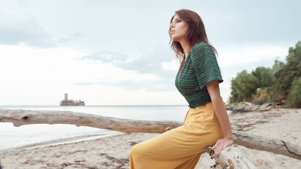Fototapeta na wymiar beautiful fashionable girl on the beach dressed in a green sweatshirt and yellow pants, stylish retro clothing, lifestyle and fashion