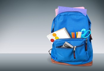 Classic school backpack with colorful school supplies and books on desk.