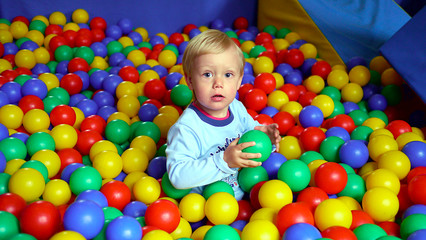 Fototapeta na wymiar Dziecko wśród kolorowych kulek na placu zabaw w bawialni, chłopiec bawi się kulkami, dziecięce zabawy wśród plastikowych kulek