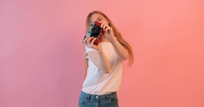 beautiful girl with a camera in her hands , on a pink background, a woman takes pictures