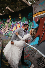 Beautiful couple having a romantic moment on their weeding day, in mountains at sunset. Happy hugging couple. Groom kissing bride. Bride is in a white wedding dress with a bouquet, groom in a suit. 