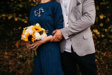 Beautiful elegant bride in blue wedding dress with long sleeves, hugged by her husband.. She is holding a big bouquet of flowers. Outdoors, on the road. Close up.