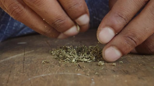 beautiful cinematic footage of a man male grinding weed marijuana cigarette joint with his hand while sitting on a bench