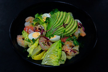 salad with avocado and shrimps in bowl, top view, copy space, black background